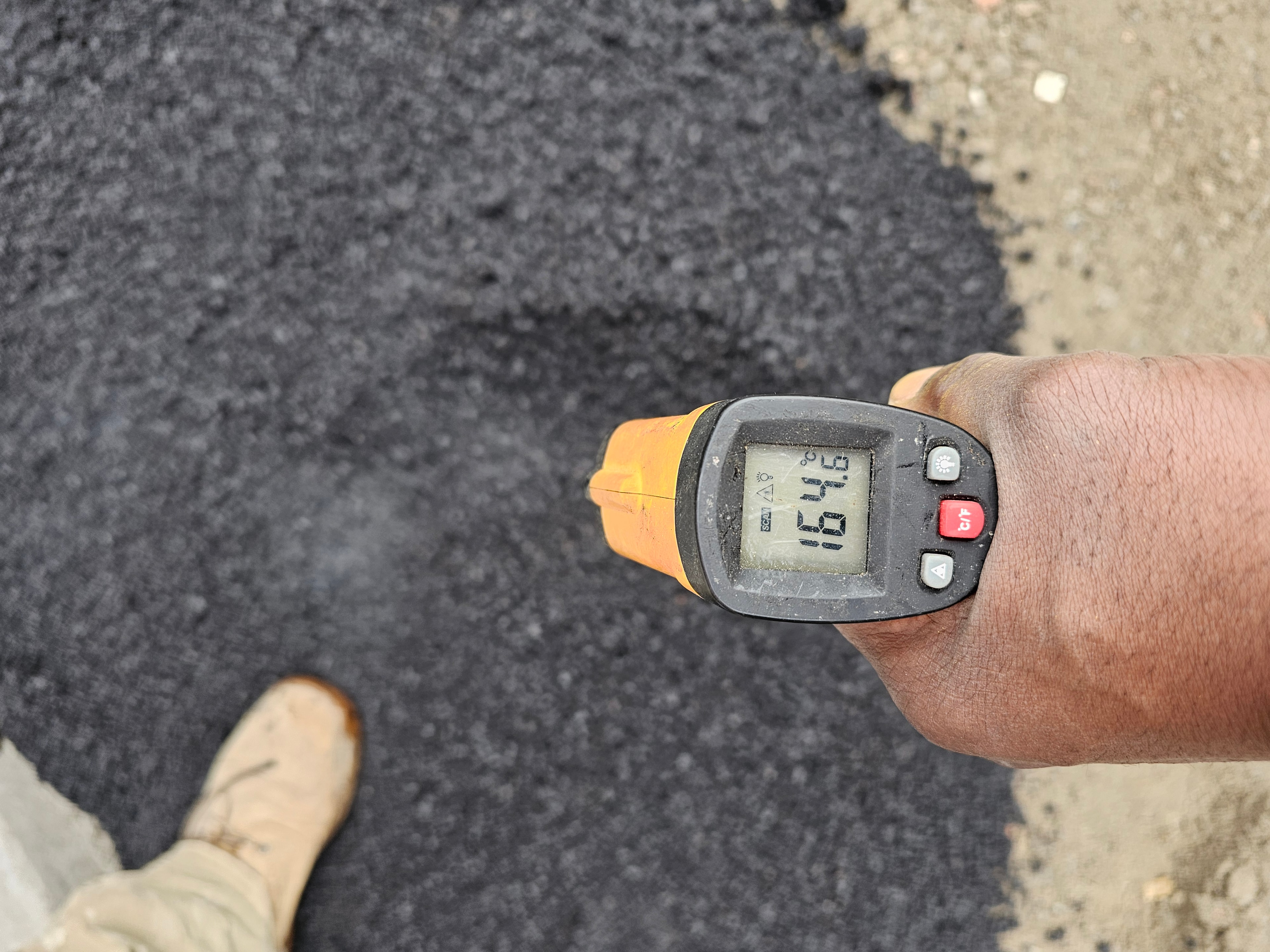 Infrared thermometer reading 164 degrees on freshly laid asphalt — quality control check