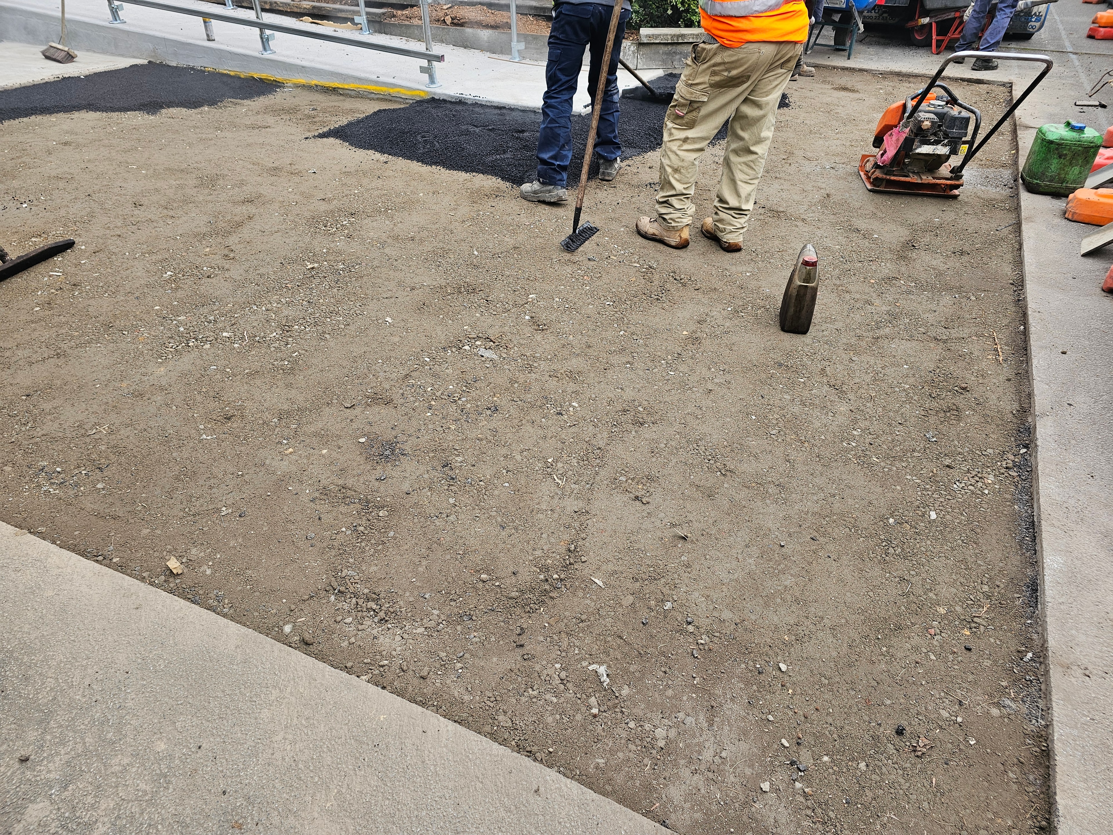BS Asphalt crew preparing base with plate compactor, fresh asphalt visible in background