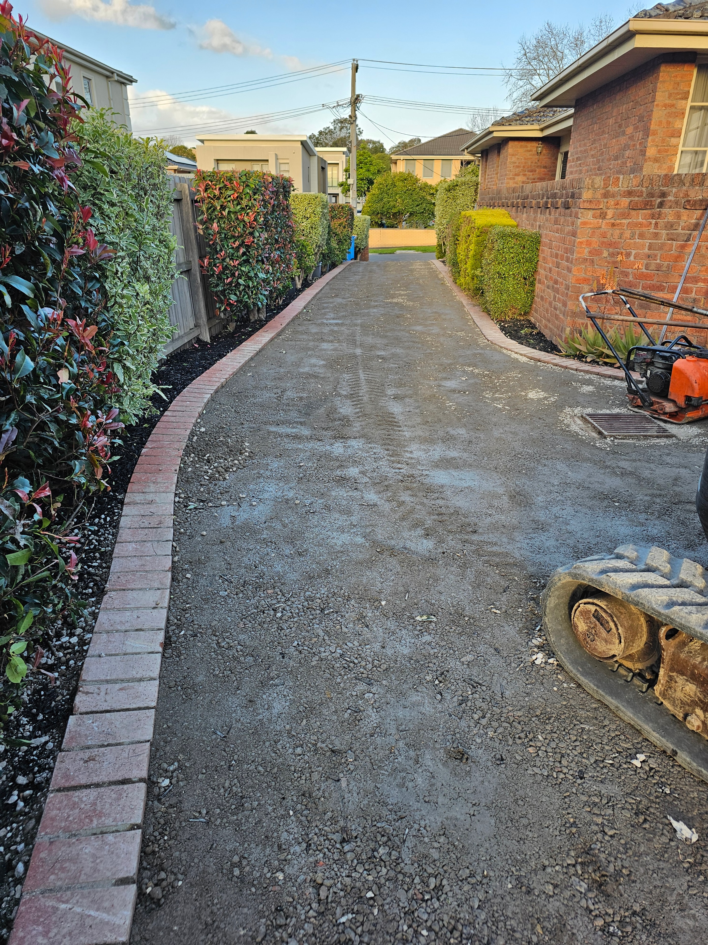 Residential driveway base preparation with roller and brick edging