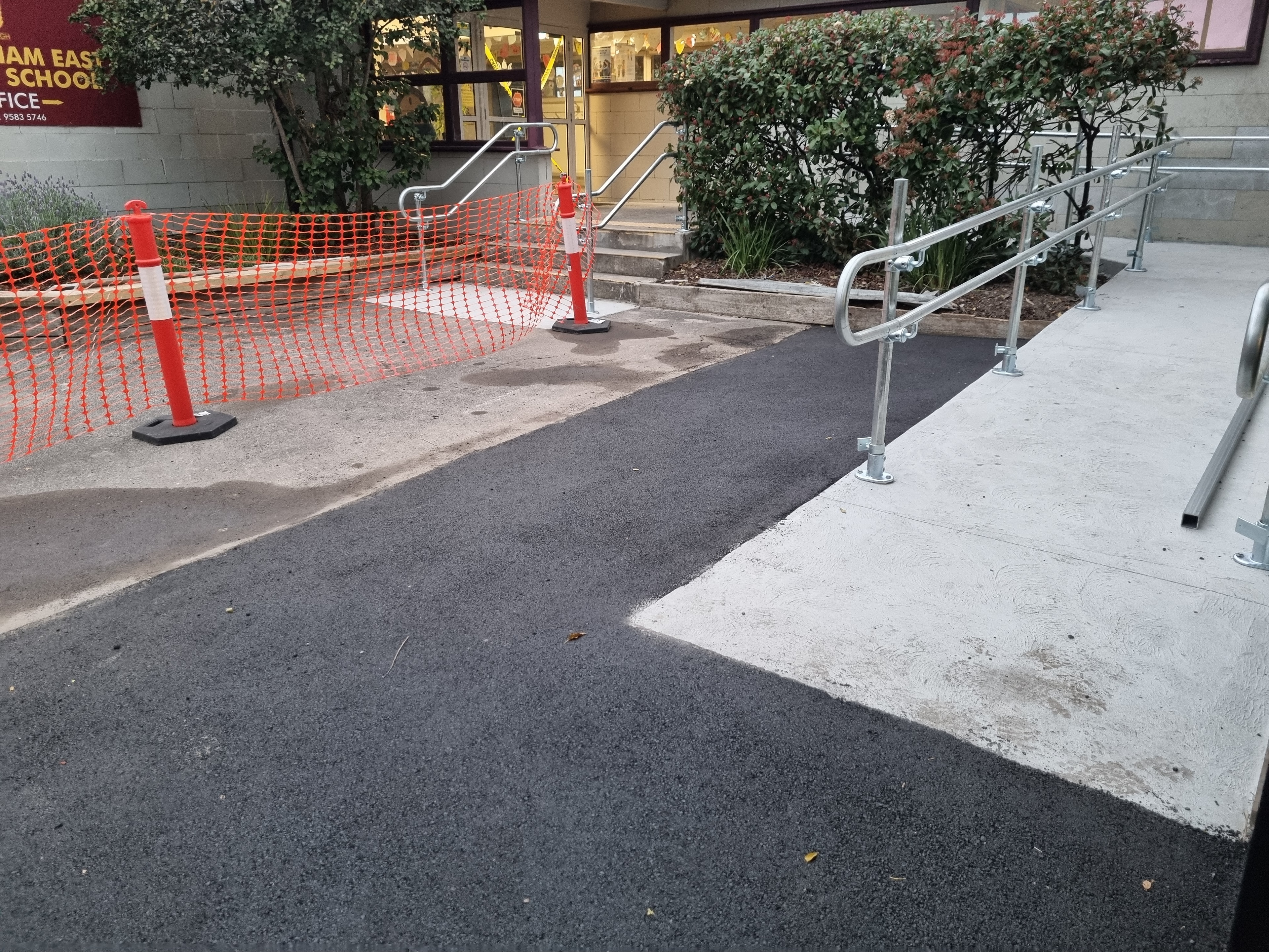Fresh asphalt footpath at school entrance with safety barriers
