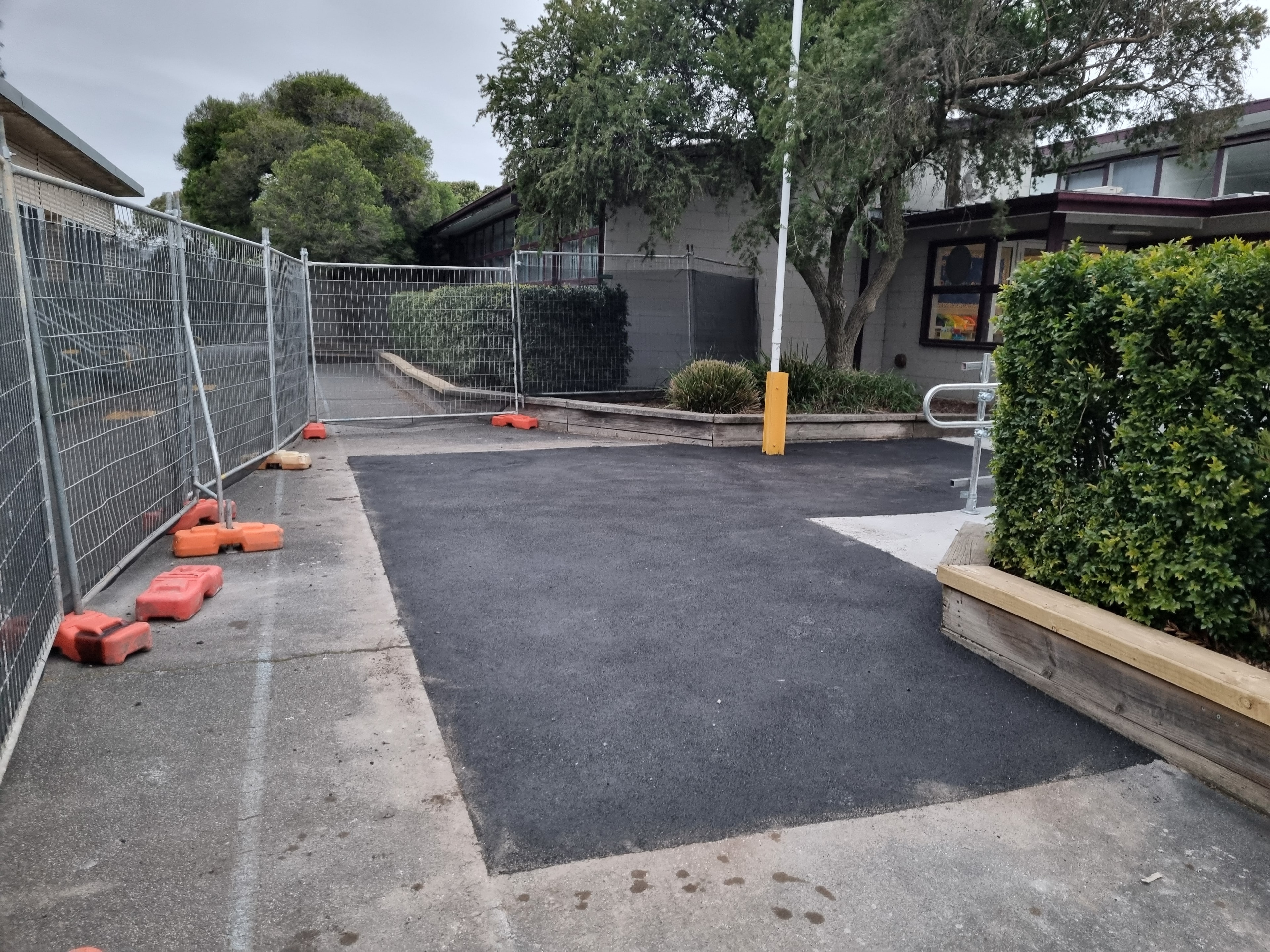 Fresh asphalt patch at school courtyard with temporary fencing
